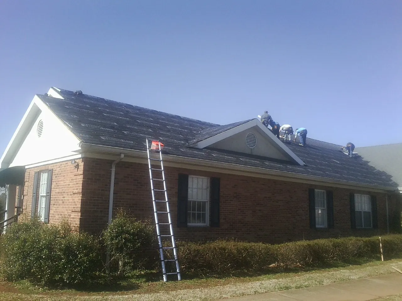 Crew tearing shingles off a brick ranch roof with a ladder set — Metal Roof Repair work by our crew in Altamont
